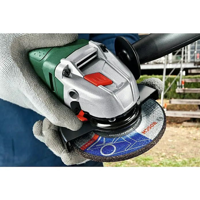 Bosch Amoladora angular eléctrica PWS 700-115 - 700 W, Diámetro disco: 115 mm, Número de revoluciones de marcha en vacío: 12.000 r.p.m. - Primer plano de una amoladora angular Bosch con disco de rectificado, sujeta con manos enguantadas. La herramienta presenta elementos verdes, plateados y negros.