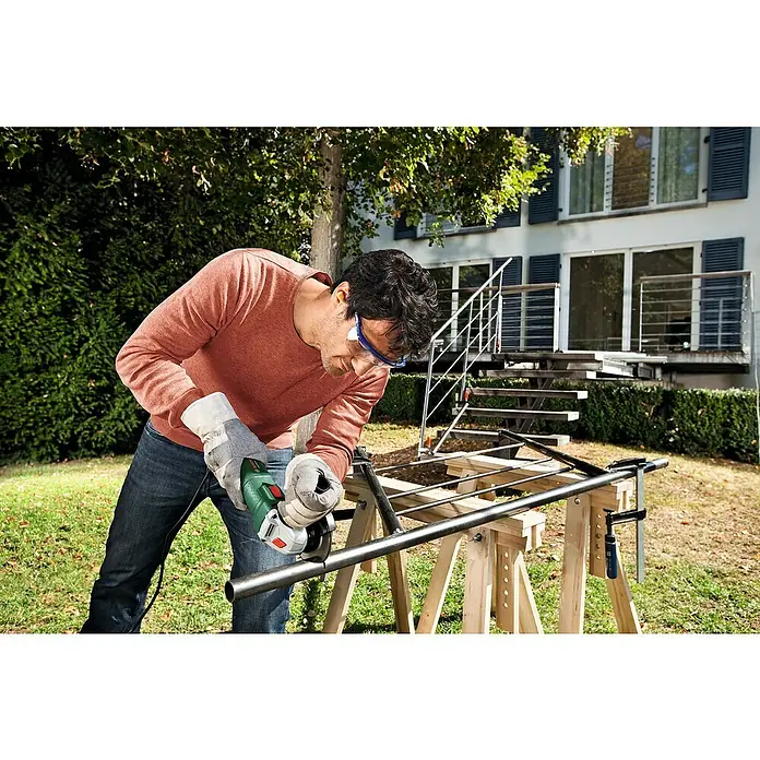Bosch Amoladora angular eléctrica PWS 700-115 - 700 W, Diámetro disco: 115 mm, Número de revoluciones de marcha en vacío: 12.000 r.p.m. - Hombre corta tubo de metal con amoladora angular al aire libre, con gafas de seguridad y guantes. Uso seguro de herramientas eléctricas.