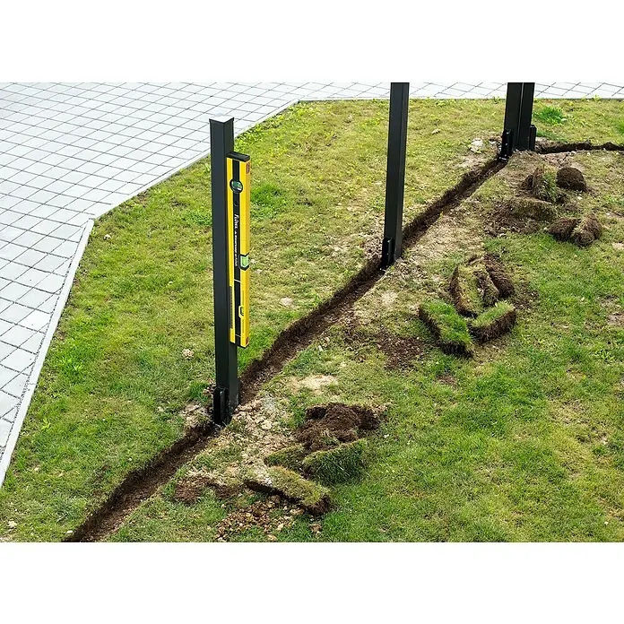 Flüwa Wasserwaage - Länge: 60 cm, Gelb/Schwarz, 16-cm-Lineal - Ein gelber Flowa Wasserwaage ist an einem schwarzen Pfosten befestigt, neben einem ausgehobenen Graben im Gras.