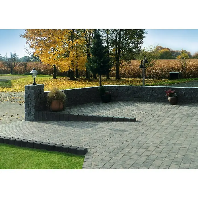 Diephaus Rechteckpalisade - 16,5 x 12 x 80 cm, Anthrazit, Beton - Außenaufnahme einer Terrasse mit Pflastersteinen und einer niedrigen Steinmauer, dekoriert mit Pflanzen in Töpfen und einer dekorativen Laterne.