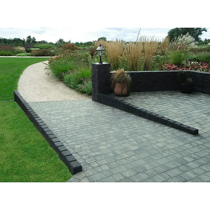 Diephaus Rechteckpalisade - 16,5 x 12 x 120 cm, Anthrazit, Beton - Eine gepflasterte Fläche mit einem dekorativen schwarzen Randstein, umgeben von Grünfläche und einem Garten mit Ziergräsern.
