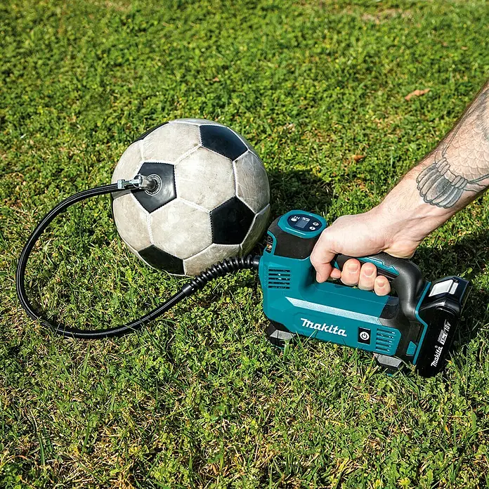 Makita LXT 18V Akku-Kompressor DMP180Z - 18 V, Ohne Akku, 8,3 bar - Luftpumpe von Makita pumpt einen Fußball auf einer Rasenfläche auf.