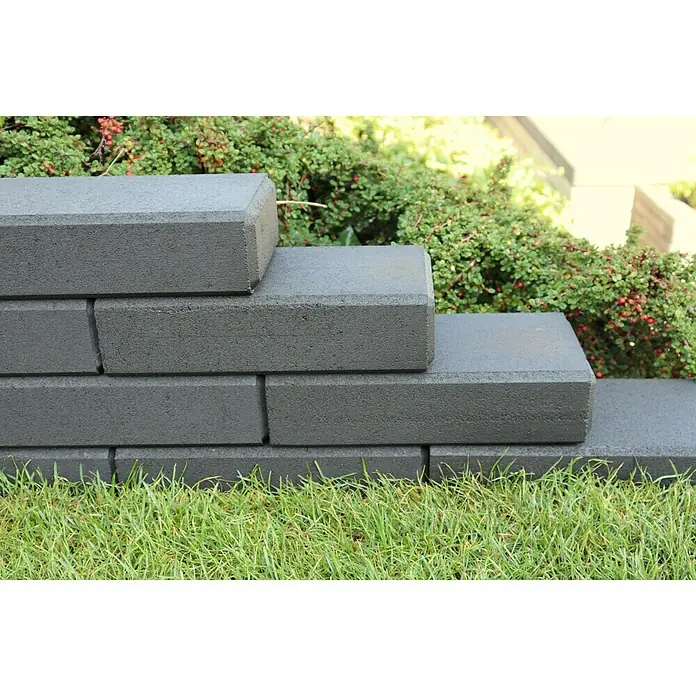 Christoph Mauerstein C-Line Block - 30 x 15 x 7,5 cm, Anthrazit, Beton - Nahaufnahme einer dekorativen, grauen Gartenmauer aus Ziegelsteinen, umgeben von üppigem Grün und Rasen.