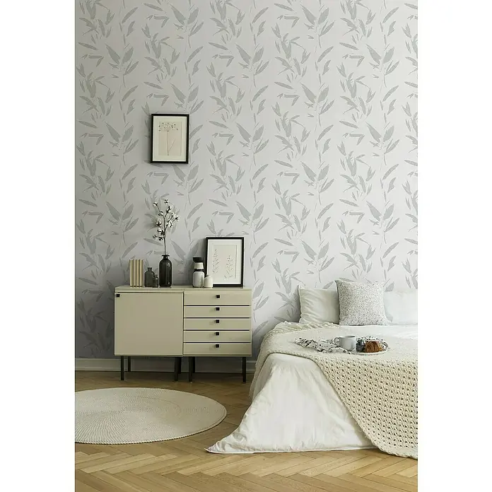 A.S. Création New Elegance Vliestapete Blätterranke - Silber, Floral, 10,05 x 0,53 m - Zimmer mit einem weißen Bett und einem modernen Beistelltisch mit grauer Blättertapete.