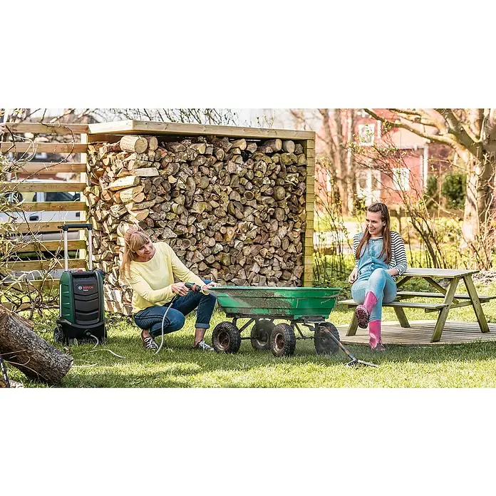 Bosch Power for All 18V Akku-Hochdruckreiniger Fontus - 18 V, 1 Akku, Max. Druck: 20 bar - Eine Frau reinigt mit einem Bosch Fontus 18V Akku-Hochdruckreiniger einen Schubkarren im Garten, während eine andere Frau zusieht.