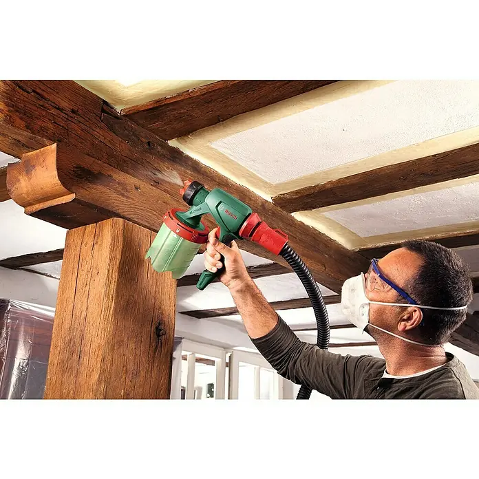 Bosch Farbsprühsystem PFS 7000 - Leistungsaufnahme: 1.400 W, Geeignet für: Alle Farbarten, 1.000 ml - Ein Mann verwendet eine Bosch Farbspritzpistole zum Streichen einer Holzbalkendecke. Das Gerät ist grün und rot.