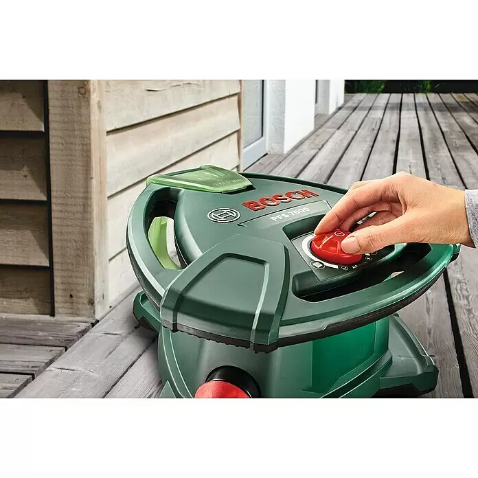 Bosch Farbsprühsystem PFS 7000 - Leistungsaufnahme: 1.400 W, Geeignet für: Alle Farbarten, 1.000 ml - Eine Hand stellt den roten 'AIR volume' Drehknopf eines dunkelgrünen Bosch PFS 7000 Farbsprühsystems ein. Das Gerät steht auf einem Holzdeck.