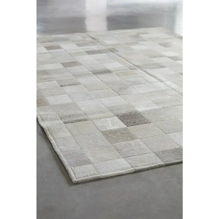 Esbeco Kuhfell Patchwork - Grau, 100 % Echtfell, 180 x 120 cm - Detailaufnahme eines grauen Teppichs mit quadratischem Patchwork-Muster, der eine elegante und moderne Ästhetik bietet.
