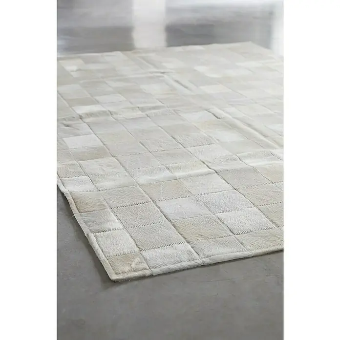 Esbeco Kuhfell Patchwork - Weiß, 100 % Echtfell, 180 x 120 cm - Nahaufnahme eines grauen Teppichs mit quadratischen Mustern, der auf einem glatten Boden liegt. Das Design des Teppichs verleiht dem Raum eine moderne Note.