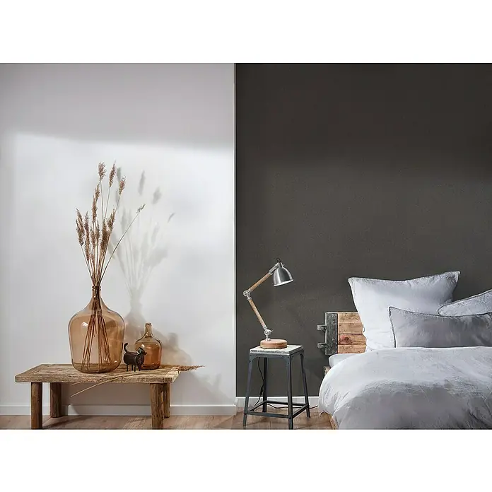 A.S. Création New Elegance Vliestapete I - Schwarz, Uni, 10,05 x 0,53 m - Nahaufnahme von Deko-Glasvasen mit Trockenblumen und einer kleinen Statue auf einem Holztisch, neben einem Bett und einer Lampe.