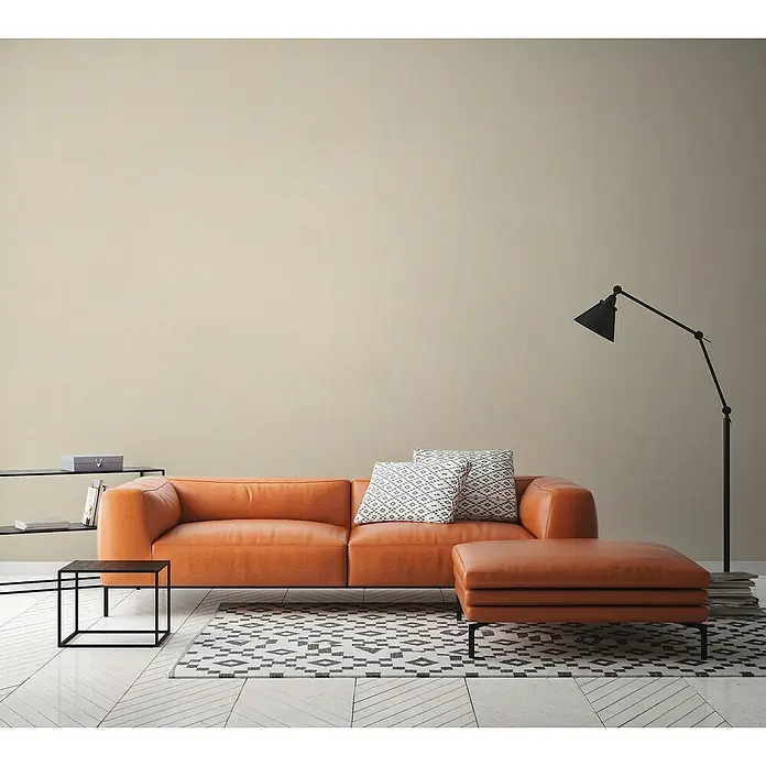 A.S. Création History of Arts Vliestapete - Creme, Uni, 10,05 x 0,53 m - Wohnzimmer mit orangefarbenem Ledersofa, passendem Hocker, schwarzer Lampe und Regal auf einem gemusterten Teppich.
