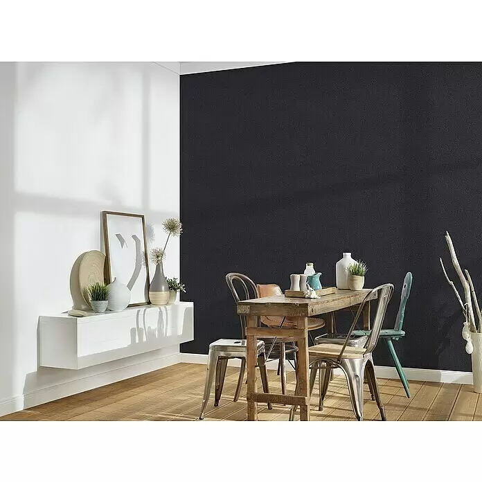 A.S. Création New Elegance Vliestapete - Schwarz, Uni, 10,05 x 0,53 m - Dunkle, subtil texturierte Tapete bedeckt eine Wand in einem Esszimmer, kontrastierend mit einer weißen Wand und Holzmöbeln.