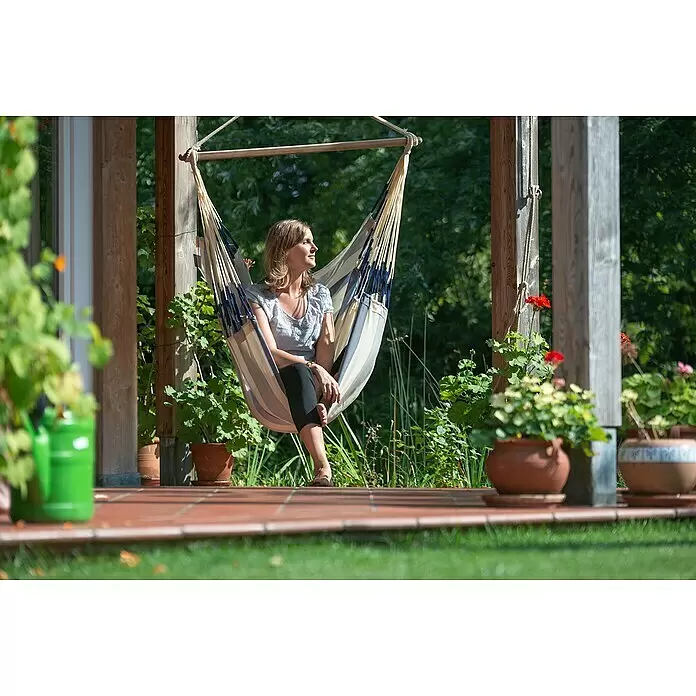 La Siesta Hamaca colgante Domingo Kingsize - L x An x Al: 210 x 130 x 170 cm, Azul/Blanco - Mujer relajándose en una silla hamaca de tela a rayas beige, azul y blanca, suspendida de una estructura de madera al aire libre.