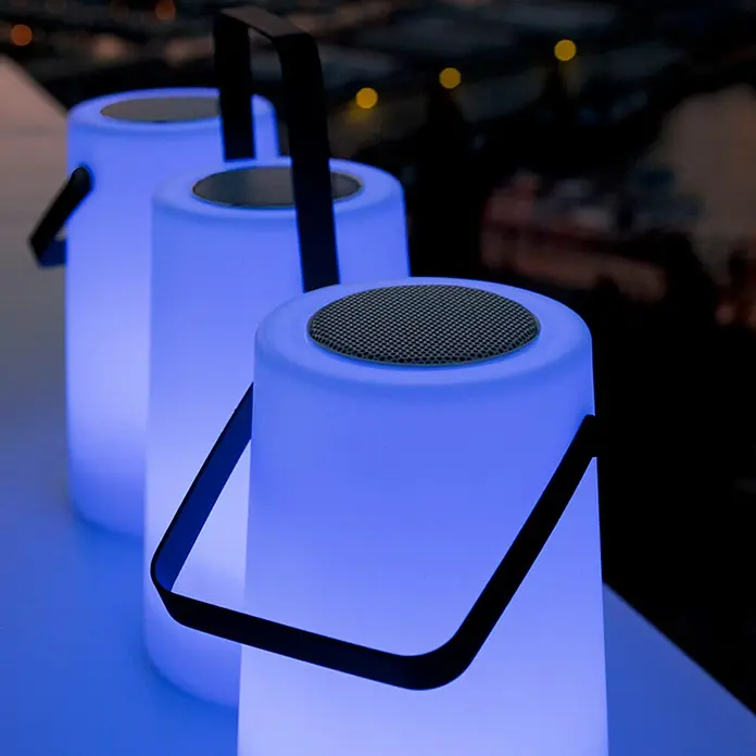 New Garden Bombilla LED Nomada play light music - Altavoz Bluetooth, 20 x 20 x 30 cm, Blanco - Tres altavoces LED portátiles con asas en fila, brillando en luz azul y creando un ambiente que crea ambiente.