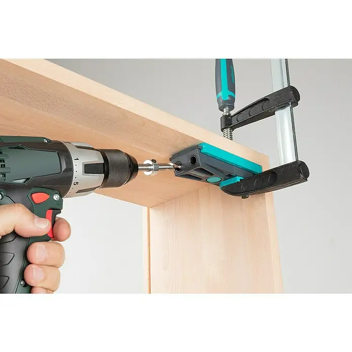 Wolfcraft Werkzeugkoffer Undercover Jig - 54 -tlg. - Eine Bohrmaschine bohrt mit einer Bohrvorrichtung Löcher in ein Holzbrett, das mit einer Zwinge fixiert ist.