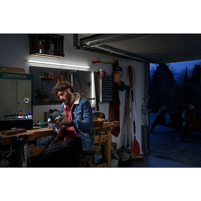 Ledvance LED-Lichtleiste Switch BattenL x B x H: 117,3 x 2,2 x 3 cm, Lichtfarbe: Warmweiß, 14 W - Ein Mann in einer Werkstatt, der an einem Motor arbeitet. Der Raum ist gut ausgestattet mit Werkzeugen und einer Werkbank, ideal für Reparaturen.