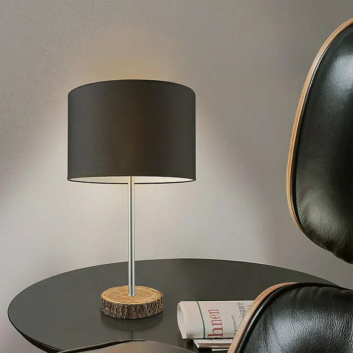 Home Sweet Home Lampenfuß Bossano - 40 W, Farbe: Braun, Höhe: 33 cm - Elegante Tischleuchte mit schwarzem Lampenschirm und Holzfuß auf einem Tisch, neben einem schwarzen Ledersessel.