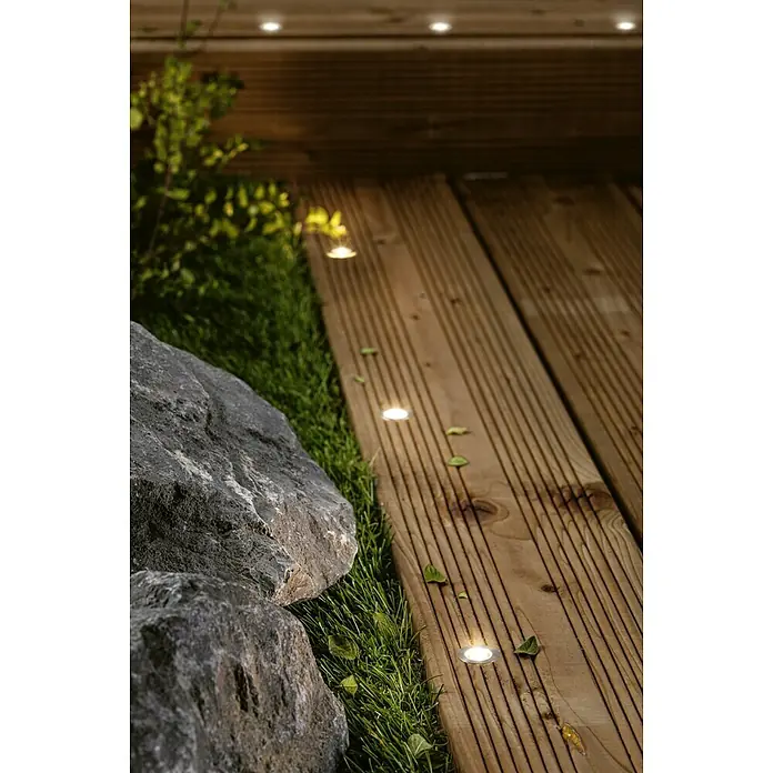 Paulmann Link & Light Bodeneinbauleuchte - 0,6 W, Silber - Eine Nahaufnahme von eingelassenen Terrassenleuchten auf einem Holzdeck neben Gras und Steinen, die eine gemütliche Außenbeleuchtung erzeugen.