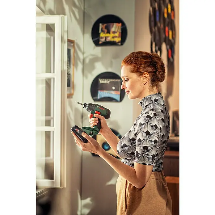 Bosch Power for All 18V Taladro atornillador percutor de batería UniversalImpact 18 - 18 V, 2 baterías, 1,5 Ah, 34 Nm - Una mujer ensamblando un taladro inalámbrico Bosch para realizar tareas de bricolaje. La herramienta es compacta e inalámbrica.