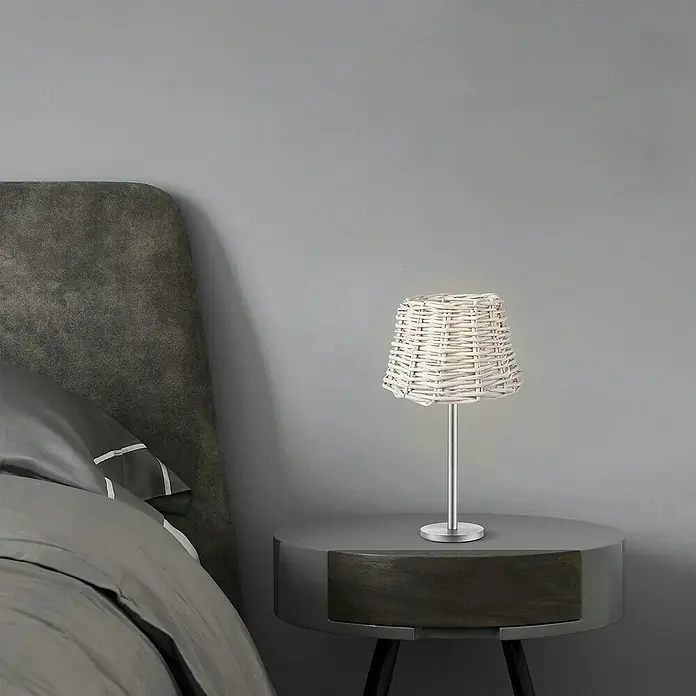 Home Sweet Home Lampenschirm Roseau - 20 cm, Weiß, Rattan, Oval - Nachttisch mit graublauem Bett und ein Korbtischlampe mit hellem Licht auf einem Nachttischschrank für eine entspannende Atmosphäre.