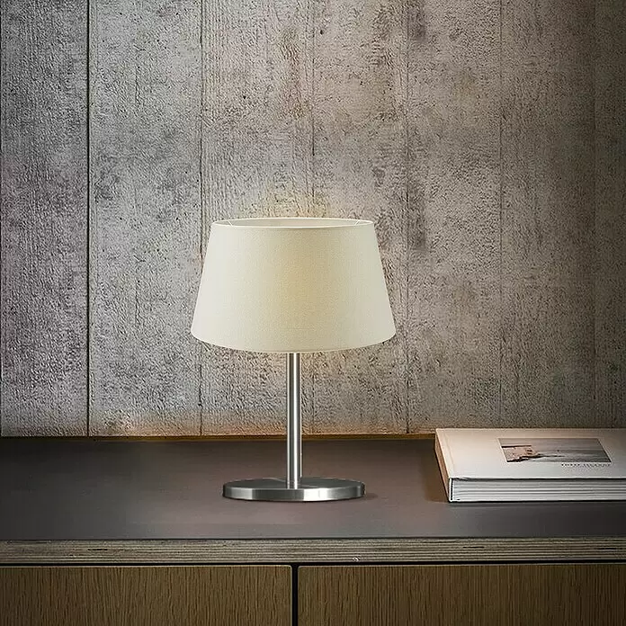 Home Sweet Home Lampenschirm Melrose - Ø x H: 35 x 19 cm, Warm White, Stoff, Rund - Creme-Stoff-Tischleuchte mit gebürstetem Metallsockel, beleuchtet einen dunklen Holztisch neben einem Buch.