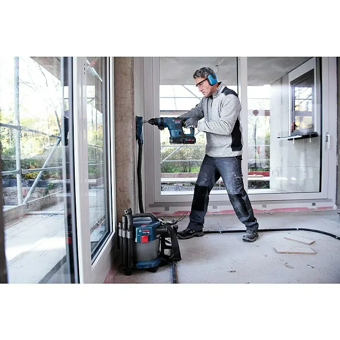 Bosch Professional AMPShare 18V Akku-Kombihammer 18V-34 CF - 18 V, Ohne Akku, 5,8 J - Ein Handwerker bohrt mit einer Bosch-Bohrmaschine ein Loch in eine Wand, während ein Staubsauger den Staub absaugt.