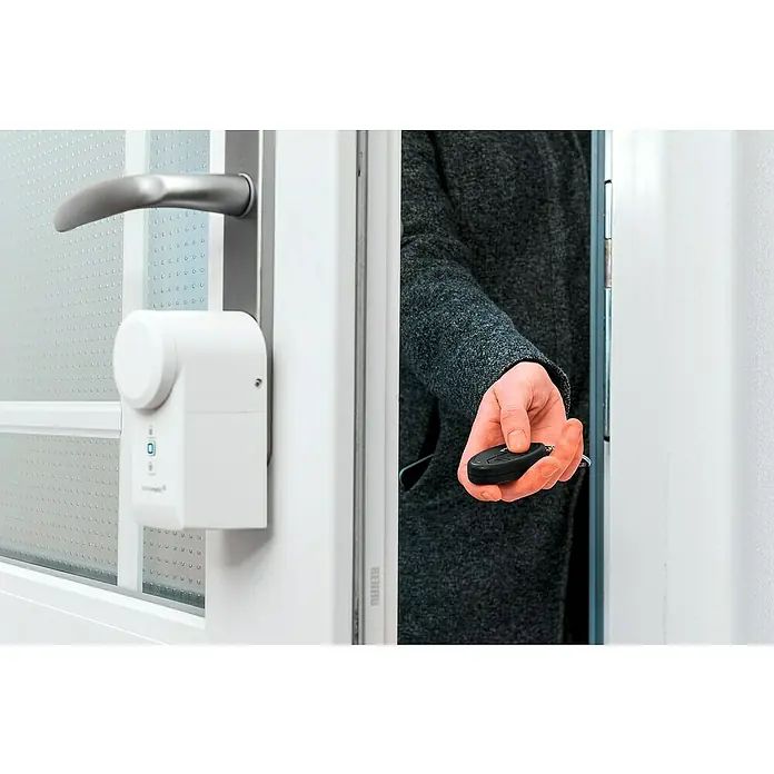 Homematic IP Funkfernbedienung HmIP-KRCK - Passend für: Homematic IP Türschlossantrieb, Schwarz, 75 x 38 x 14 mm - Smarte Türöffnung: Eine Hand hält eine Fernbedienung vor einer Tür mit installiertem, intelligentem Türschloss für schlüssellosen Zugang.