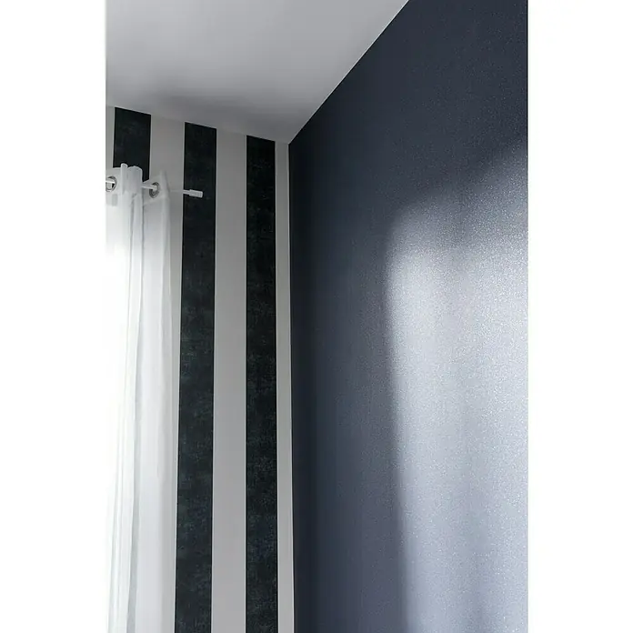 A.S. Création Vliestapete Life 2 - Schwarz/Metallic, Uni, 10,05 x 0,53 m - Zimmerinneneinrichtung mit einer Wand mit grauen und weißen Streifen und einer dunkelgrauen Wand, die ein modernes Design zeigt.