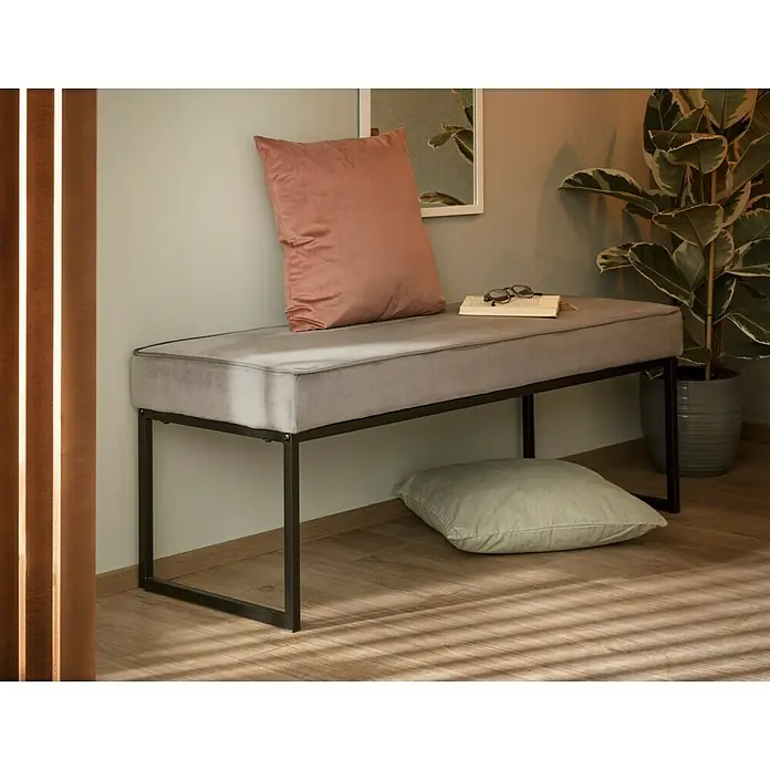 SCHÖNER WOHNEN-Kollektion Vliestapete Unistruktur - Olivgrün, Uni, 10,05 x 0,53 m - Eine stilvolle, graue Bank mit einem rosafarbenen Kissen und einem zusätzlichen Kissen darunter, ideal für ein modernes Interieur.