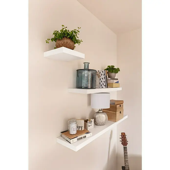 Regalux Wandboard XL4 - L x B x H: 23,5 x 118 x 3,8 cm, Weiß, Belastbarkeit: 12 kg - Wandregale mit dekorativen Gegenständen wie Pflanzen, einer Lampe und Büchern. Die Regale sind weiß und an einer hellen Wand befestigt.