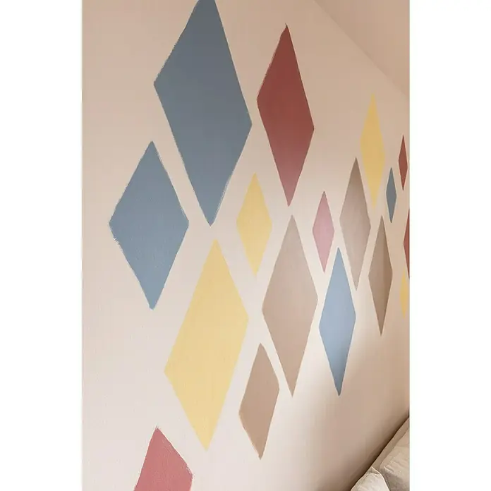 SCHÖNER WOHNEN-Farbe Wandfarbe Designfarbe - Leichtes Leinenbeige, Matt, 2,5 l, Konservierungsmittelfrei - Eine Wand mit farbenfrohen, handgemalten Rauten in verschiedenen Größen, die ein spielerisches und modernes Muster erzeugen.