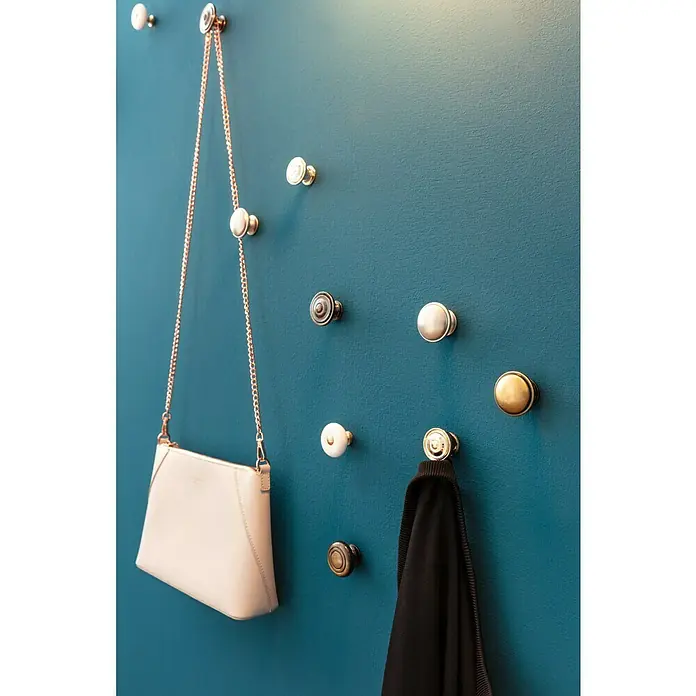 swingcolor Farbtester SIMPLY Wohnraumfarbe - Blau - Nr. 18, Matt, 50 ml - Wandgarderobe mit verschiedenen Knöpfen an einer blaugrünen Wand, eine Handtasche und ein Kleidungsstück hängen daran.