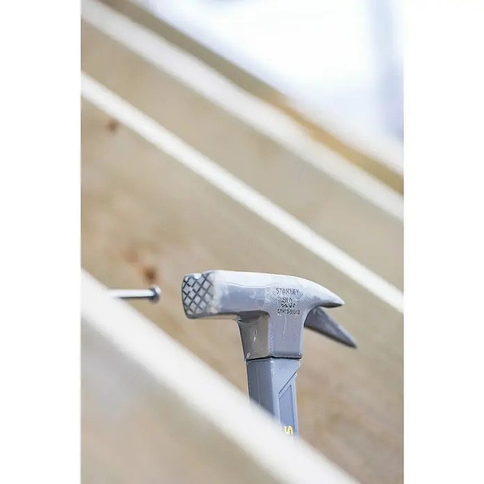 Stanley Zimmermannshammer STHT0-51312 - Gewicht Kopf: 600 g, Geraute Bahn - Nahaufnahme eines Stanley-Hammers, der auf Holzbalken liegt, mit einem Nagel in der Nähe, ideal für Bau- oder Heimwerkerprojekte.