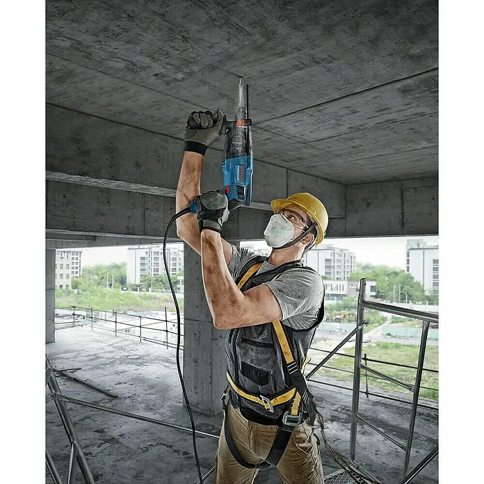 Bosch Professional Kombihammer GBH 2-21 - 720 W, 2 J, SDS-Plus-Aufnahme, Inkl. Koffer - Ein Bauarbeiter benutzt einen Bosch-Bohrhammer mit Staubabsaugung, um ein Loch in eine Betondecke zu bohren.