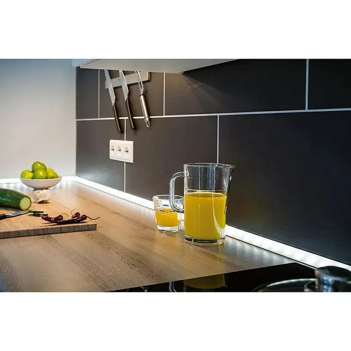 Paulmann Delta Perfil Difusor - 1 m, Plástico - Escena de cocina luminosa con un vaso y una jarra de zumo de naranja sobre una encimera de madera, iluminada por tiras LED bajo los armarios.