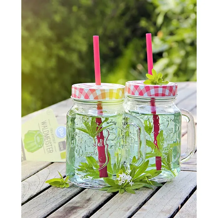 Blu Bio Waldmeister - Galium odoratum - Waldmeister-Getränk in zwei Gläsern mit rotem Strohhalm und kariertem Deckel, auf einem Holztisch im Grünen. Erfrischend und einladend!