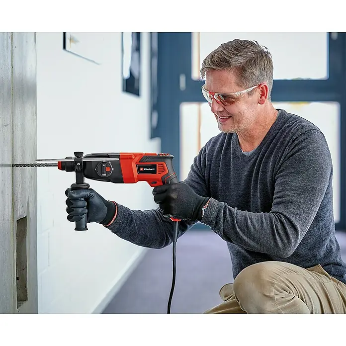 Einhell Classic Kombihammer TC-RH 620 4F - 620 W, 2,2 J, SDS-Plus-Aufnahme - Mann bohrt mit einer Einhell-Bohrmaschine ein Loch in eine Wand. Die Bohrmaschine ist rot und schwarz und der Mann trägt eine Schutzbrille.