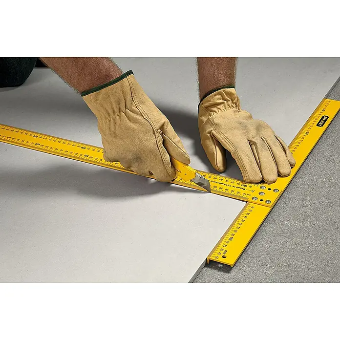 Stanley Winkelmesser - Länge: 122 cm - Gelber Stanley-Winkel mit Markierungen, der zum Zuschneiden eines Werkstücks mit einem gelben Universalmesser verwendet wird, während Handschuhe getragen werden.