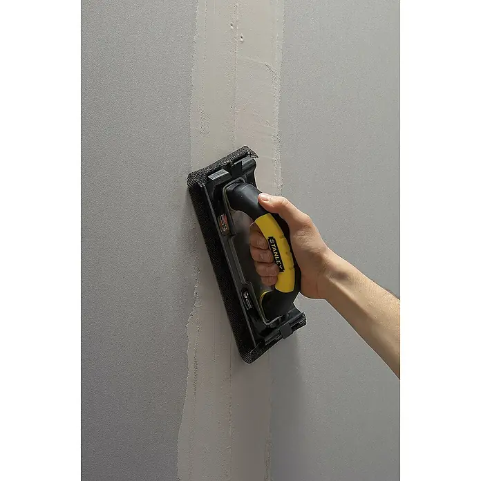 Stanley Handschleifer - Maße Handschleifer: 230 x 80,4 mm - Handwerker schleift mit einem Stanley Handschleifer eine Wand, um sie für die weitere Bearbeitung vorzubereiten.