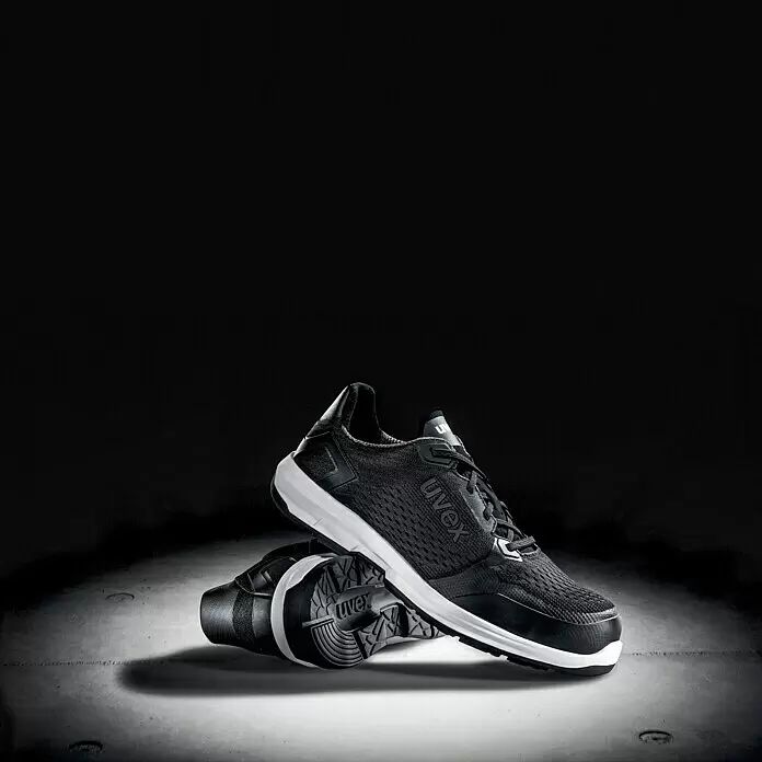 Uvex Sicherheitshalbschuh 1 Sport - 45, Schutzklasse nach EN ISO 20345: S1 - Paar schwarze Uvex Sicherheits-Sneaker mit weißer Zwischensohle, einer stehend, einer die schwarze Laufsohle zeigend.