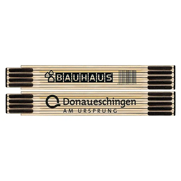 BAUHAUS Zollstock - DONAUESCHINGEN - Zwei Zollstöcke, einer mit dem Bauhaus-Logo und der andere mit dem Donaueschingen-Logo, liegen übereinander auf schwarzem Hintergrund.