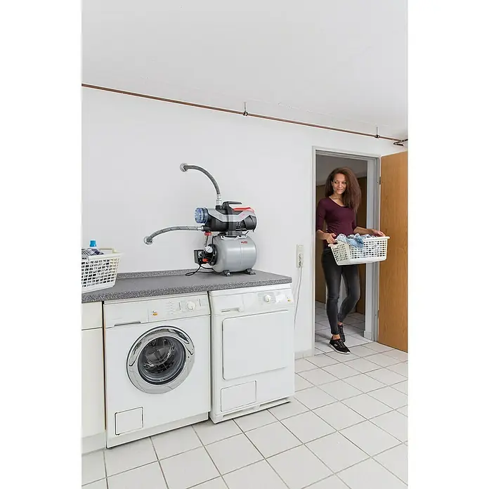 AL-KO Easy Hauswasserwerk 3600 - 850 W, Max. Fördermenge: 3.600 l/h, Max. Druck: 3,8 bar - Eine AL-KO Hauswasseranlage steht auf einer Arbeitsfläche neben Waschmaschine und Trockner in einem hellen Waschraum.