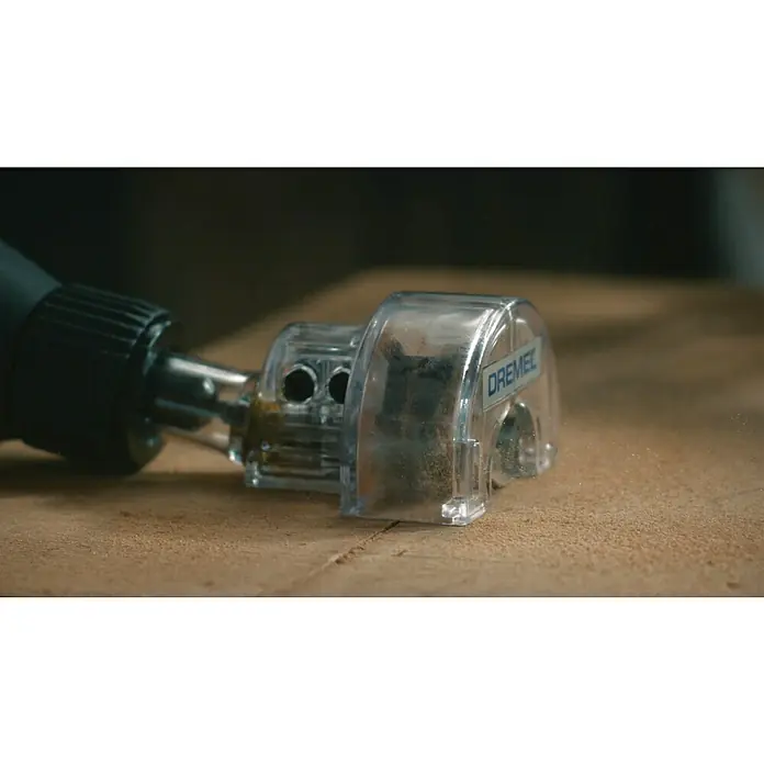 Dremel Kreissäge-Vorsatz Mod. 670 - Schnitttiefe: 6,4 mm - Nahaufnahme eines Dremel-Werkzeugs mit einem klaren Aufsatz zum präzisen Schneiden auf einer Holzoberfläche. Das Werkzeug scheint in Gebrauch zu sein.