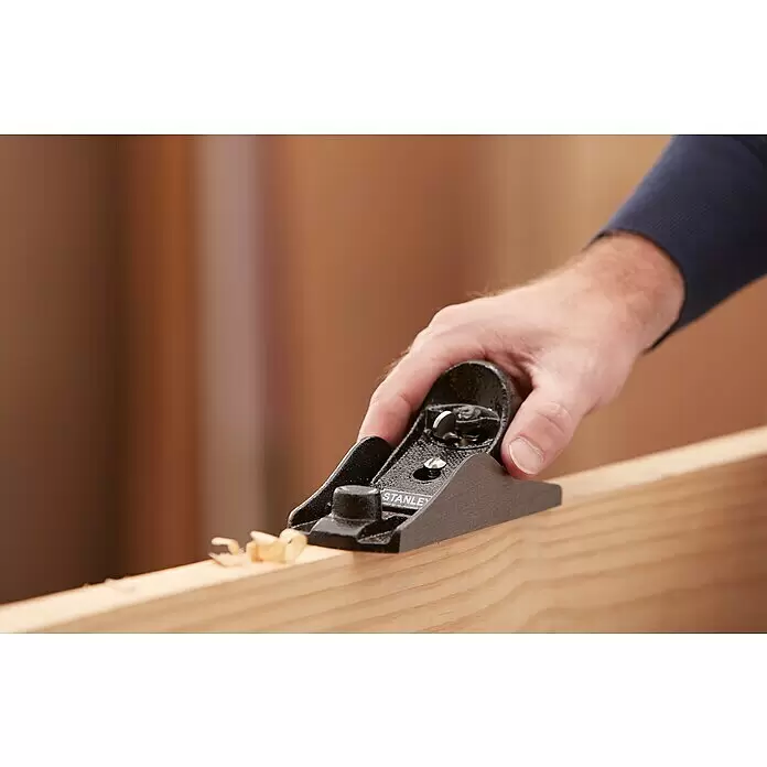 Stanley Hobel Nr. 220 - Schneidwinkel: 21 ° - Eine Hand hobelt mit einem schwarzen Stanley-Hobel ein helles Holzbrett, feine Holzspäne sind sichtbar.