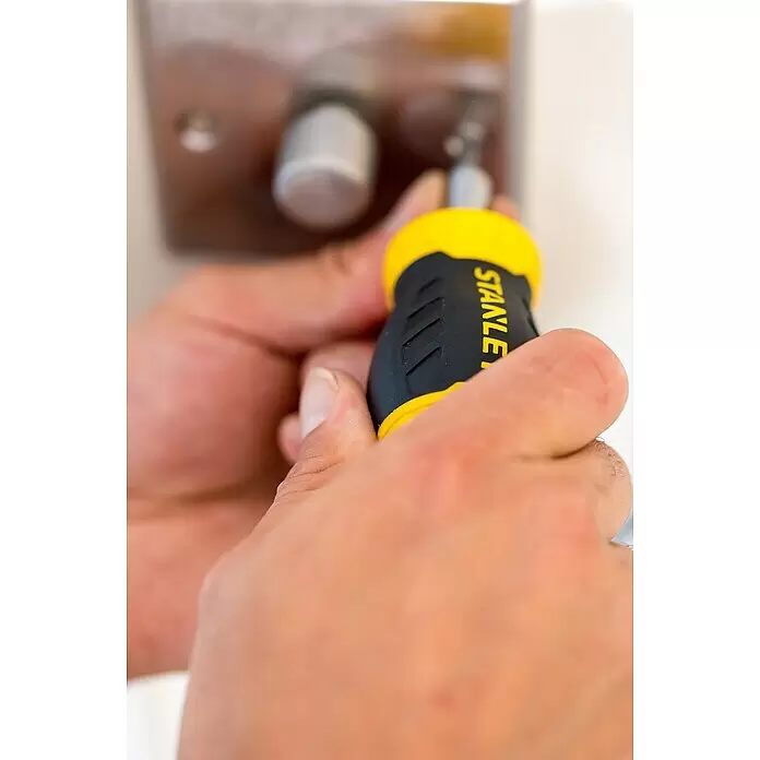 Stanley Vergaser Schraubendreher Stubby 0-66-357 - 8 -tlg. - Hände halten einen schwarz-gelben Stanley-Schraubendreher und drehen eine Schraube an einem Türschloss.