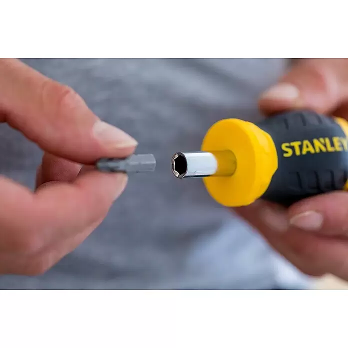 Stanley Vergaser Schraubendreher Stubby 0-66-357 - 8 -tlg. - Eine Hand hält einen grauen Schraubendreherbit und ist dabei, ihn in den Sechskantantrieb eines gelb-schwarzen Stanley Schraubendrehers einzuführen.