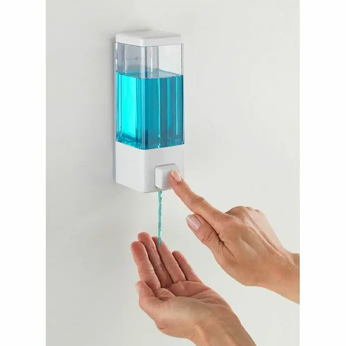 Wenko Dispensador de jabón o gel desinfectante Istres - Plástico, Blanco, Capacidad del depósito: 320 ml - Un dispensador de jabón de pared con una mano que lo acciona para dispensar jabón azul en la mano que se sujeta debajo.