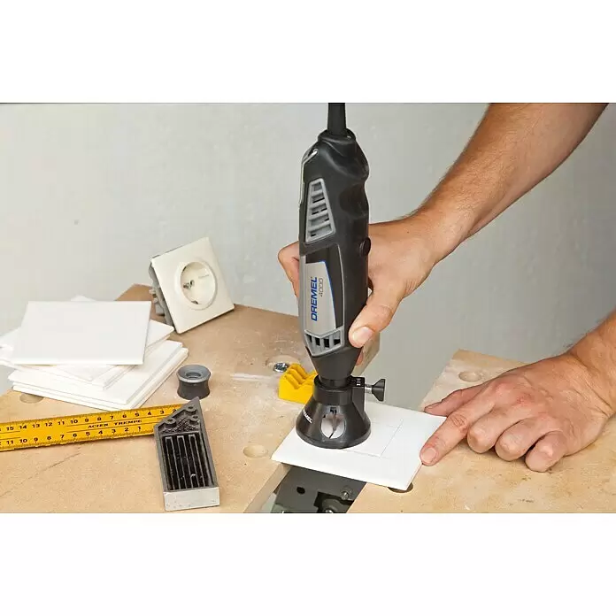 Dremel Fräsvorsatz Mod. 566 - Geeignet für: Keramikfliesen, Arbeitstiefe: 19 mm - Ein Dremel 4000 Rotationswerkzeug mit Fräsvorsatz wird verwendet, um eine weiße Fliese präzise auf einer Werkbank zu schneiden.
