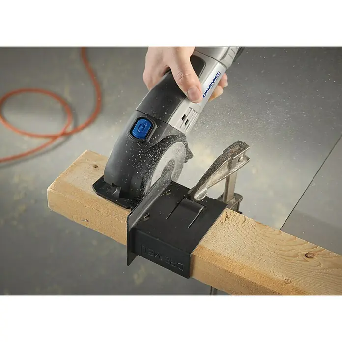 Dremel Karbid-Trennscheibe DSM 600 - Durchmesser Scheibe: 77 mm, Schnitttiefe: 20 mm - Nahaufnahme einer Dremel Kreissäge beim Schneiden eines Holzstücks, das mit einer Zwinge fixiert ist. Staubpartikel sind in der Luft sichtbar.