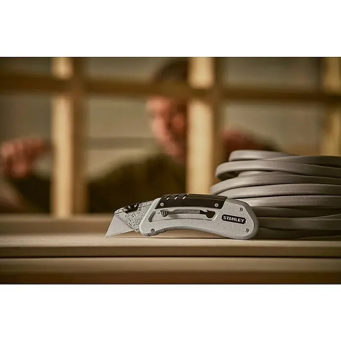 Stanley Taschenmesser Quickslide - 8,7 cm, Silber/Schwarz - Nahaufnahme eines Stanley-Messers auf einer Werkbank, das sich ideal zum Schneiden von Materialien bei Bauprojekten eignet.